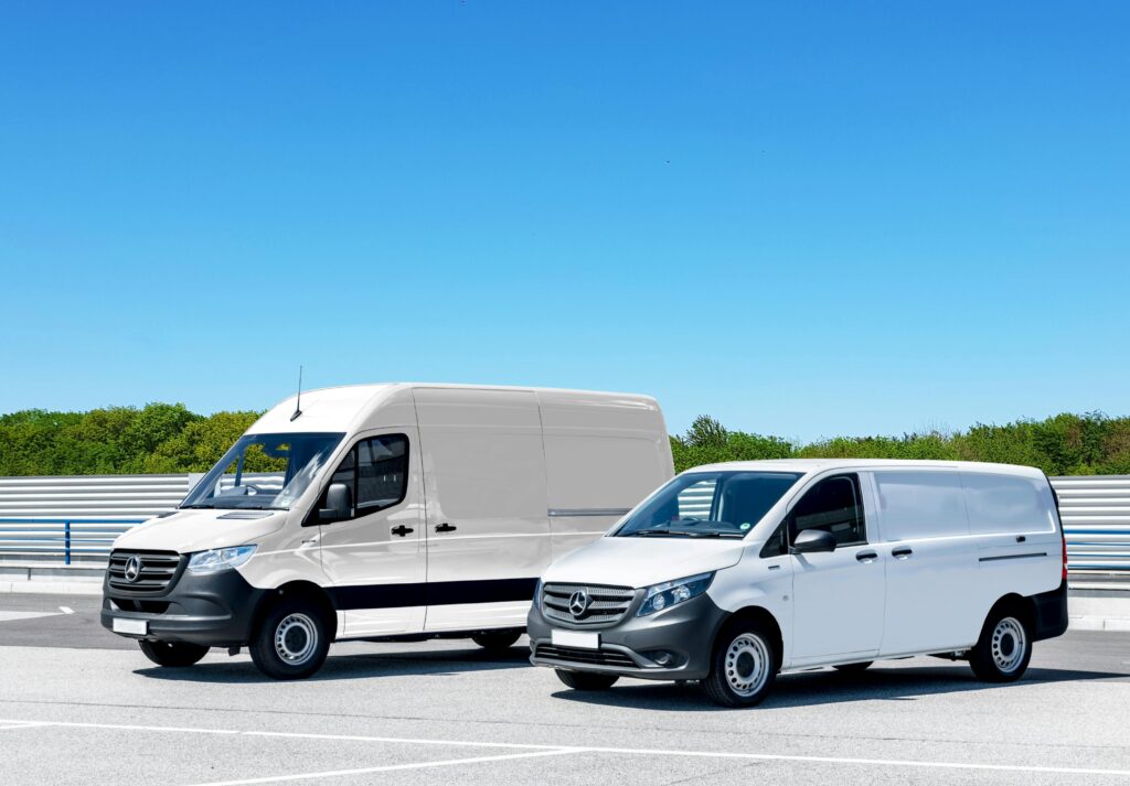 pexels-photo-4620555-4620555 Two white delivery vans parked in a spacious parking lot under a clear blue sky.
